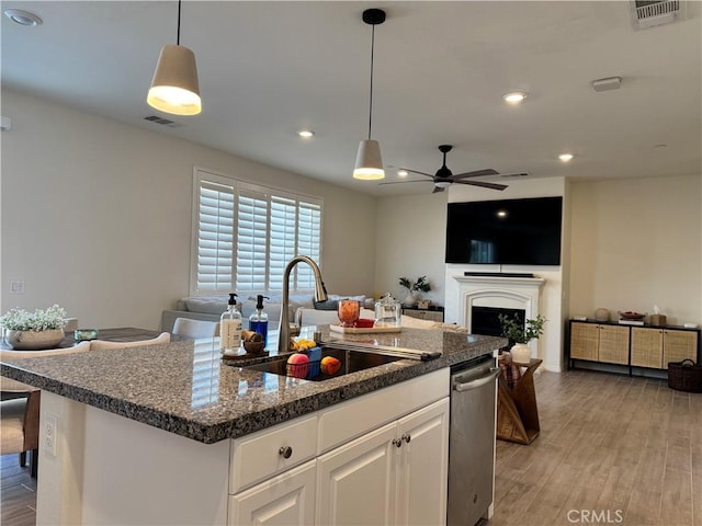 kitchen featuring a kitchen island with sink, sink, white cabinets, and decorative light fixtures