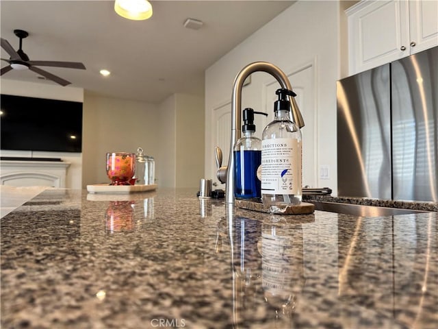 kitchen featuring white cabinetry, stainless steel fridge, ceiling fan, and dark stone counters