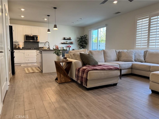 living room featuring sink, light hardwood / wood-style flooring, and ceiling fan