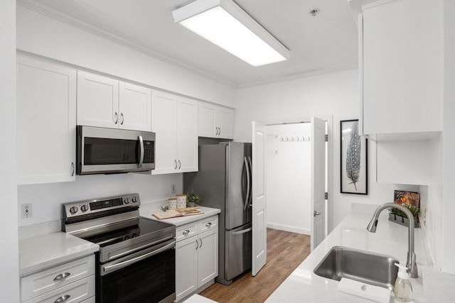 kitchen with sink, white cabinets, ornamental molding, stainless steel appliances, and light hardwood / wood-style flooring