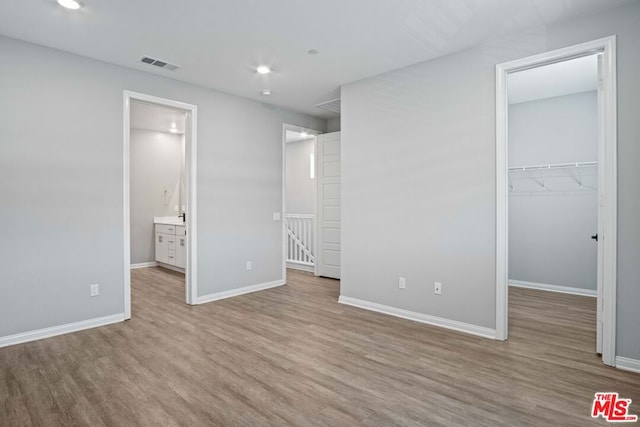 unfurnished bedroom featuring a closet, a walk in closet, ensuite bathroom, and light hardwood / wood-style flooring