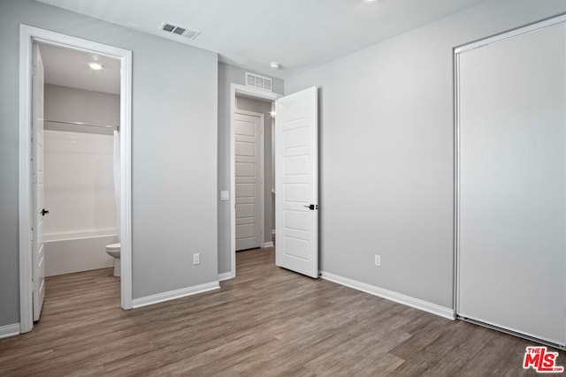 unfurnished bedroom featuring a closet, ensuite bathroom, and light wood-type flooring