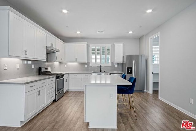 kitchen with sink, a breakfast bar area, stainless steel appliances, white cabinets, and a kitchen island