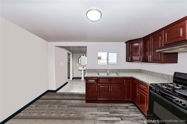 kitchen with light stone countertops, black gas range oven, sink, and light hardwood / wood-style flooring