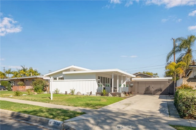 view of front facade featuring concrete driveway, fence, and a front lawn