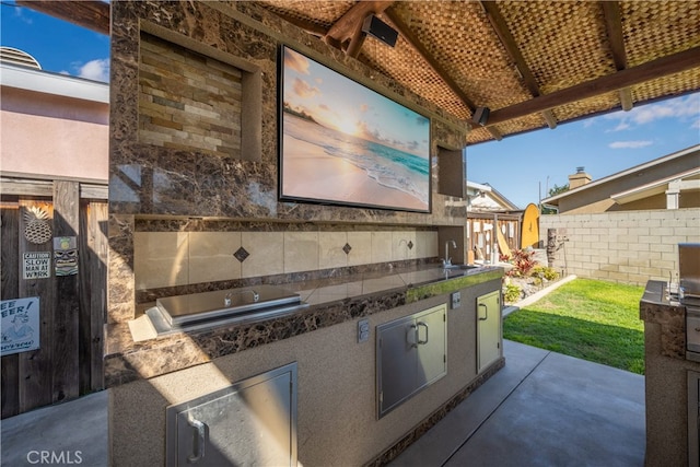 view of patio featuring a sink, an outdoor kitchen, and fence