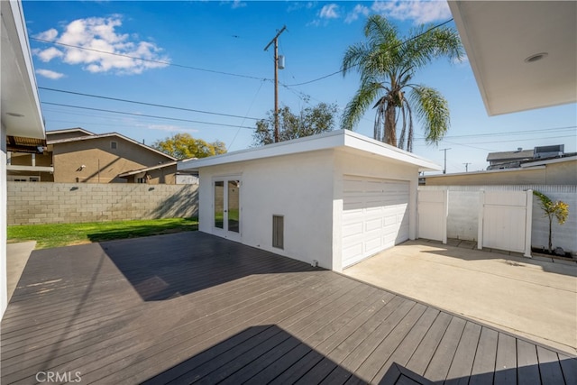 wooden deck with driveway, a garage, fence, and an outbuilding