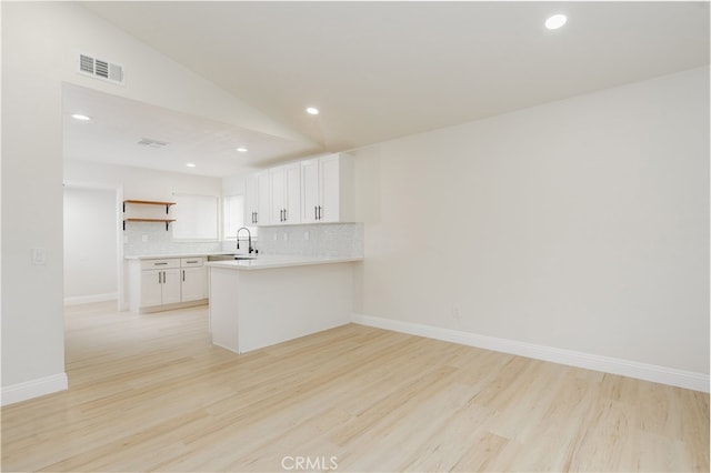 kitchen featuring tasteful backsplash, white cabinetry, light hardwood / wood-style flooring, and kitchen peninsula