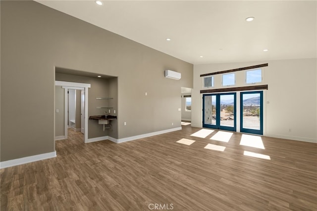 unfurnished living room featuring hardwood / wood-style flooring, high vaulted ceiling, a wall unit AC, and french doors