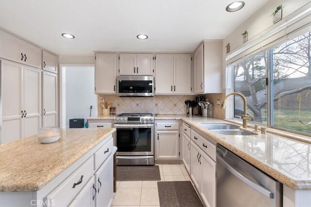 kitchen featuring sink, light tile patterned floors, white cabinetry, stainless steel appliances, and a center island