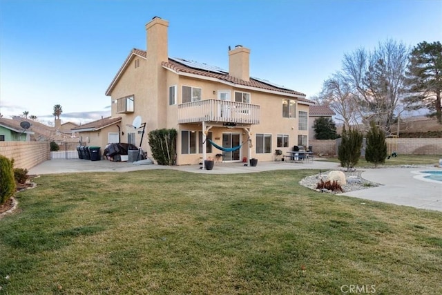 rear view of property featuring a balcony, a yard, a patio, and solar panels