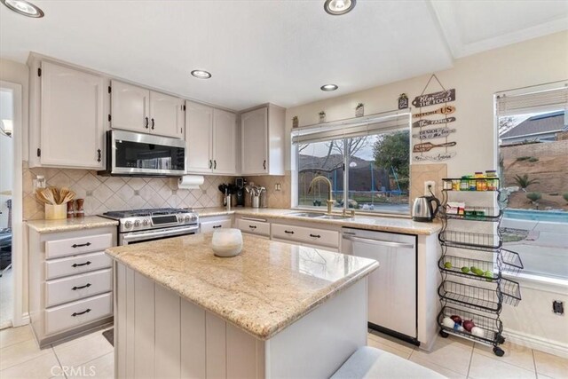 kitchen with stainless steel appliances, light stone countertops, a kitchen island, and sink