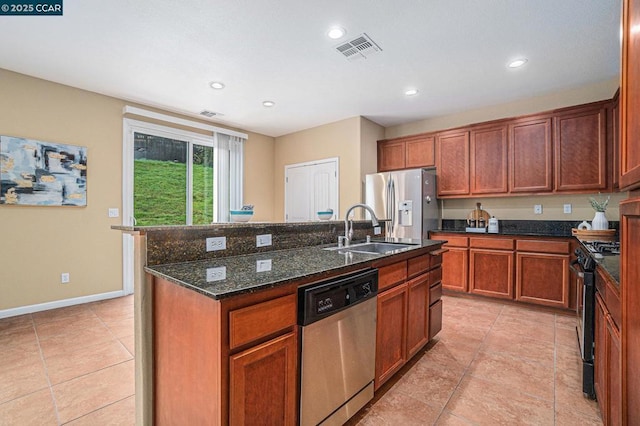 kitchen with light tile patterned flooring, sink, dark stone counters, stainless steel appliances, and a kitchen island with sink