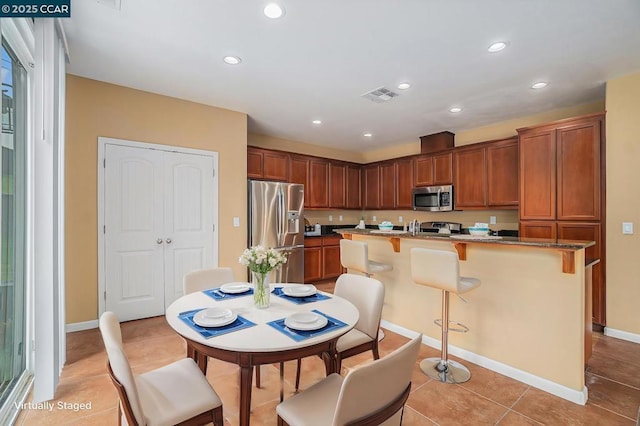 kitchen featuring light tile patterned flooring, stainless steel appliances, an island with sink, and a breakfast bar area