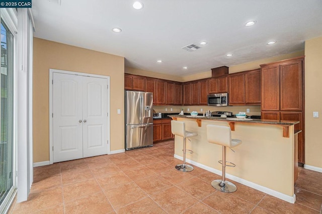 kitchen featuring stainless steel appliances, a kitchen island with sink, light tile patterned floors, and a kitchen breakfast bar