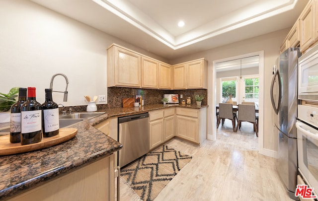 kitchen featuring sink, light hardwood / wood-style flooring, backsplash, stainless steel appliances, and a tray ceiling