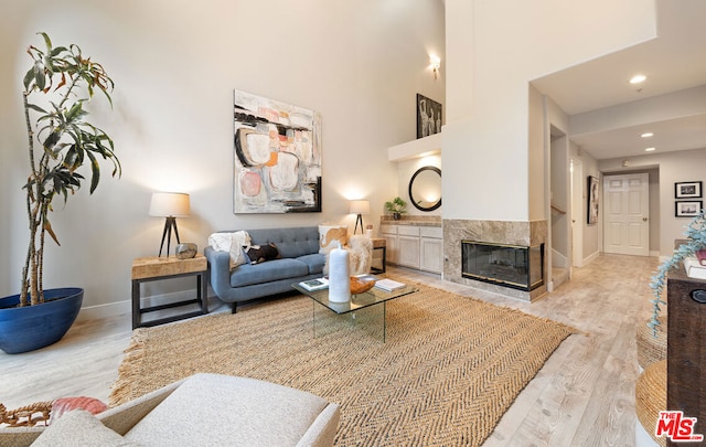 living room with a premium fireplace, a towering ceiling, and light wood-type flooring