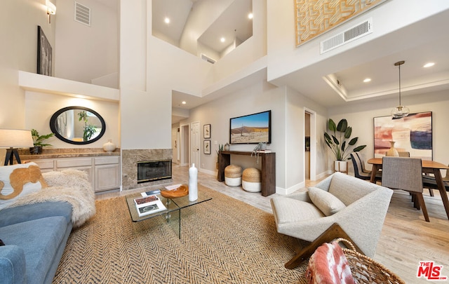 living room with a high end fireplace, light hardwood / wood-style flooring, and a high ceiling