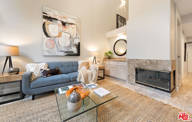 living room featuring light hardwood / wood-style floors, a tile fireplace, and a high ceiling