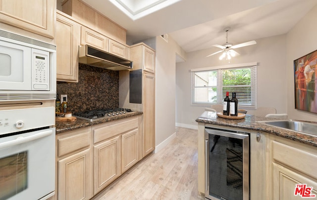 kitchen featuring backsplash, wine cooler, dark stone counters, white appliances, and light hardwood / wood-style flooring