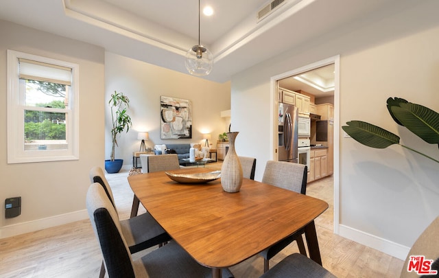 dining space with light hardwood / wood-style floors and a raised ceiling