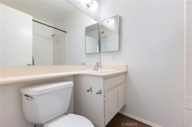 bathroom with wood-type flooring, vanity, tiled shower, and toilet