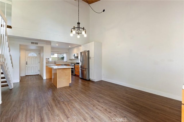 kitchen featuring white cabinetry, decorative light fixtures, a kitchen island, appliances with stainless steel finishes, and dark hardwood / wood-style floors