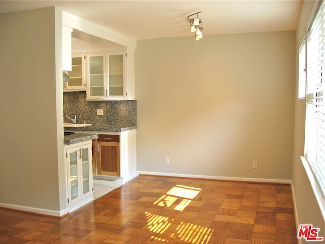 kitchen featuring light stone countertops, parquet floors, white cabinets, and decorative backsplash