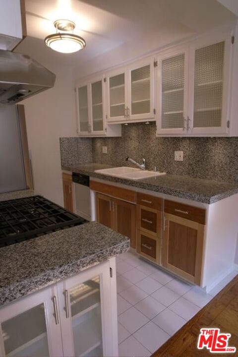 kitchen with tasteful backsplash, white cabinetry, dishwasher, sink, and light stone counters