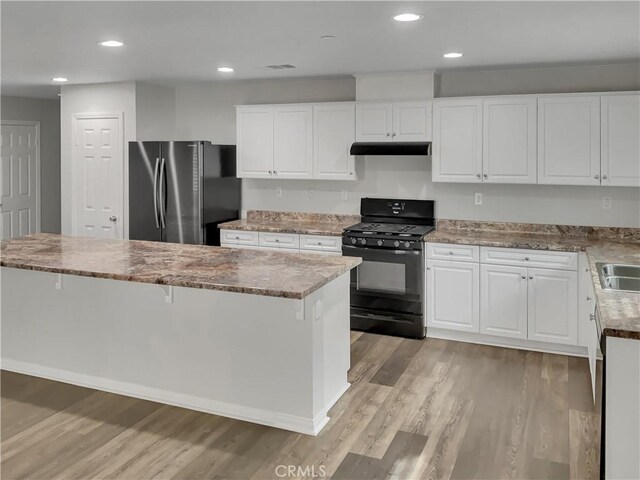 kitchen featuring a kitchen breakfast bar, stainless steel refrigerator, white cabinets, and black gas stove