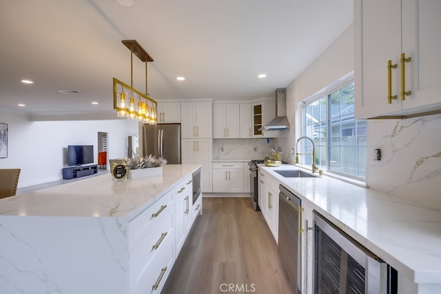 kitchen with wall chimney exhaust hood, sink, white cabinetry, hanging light fixtures, and appliances with stainless steel finishes