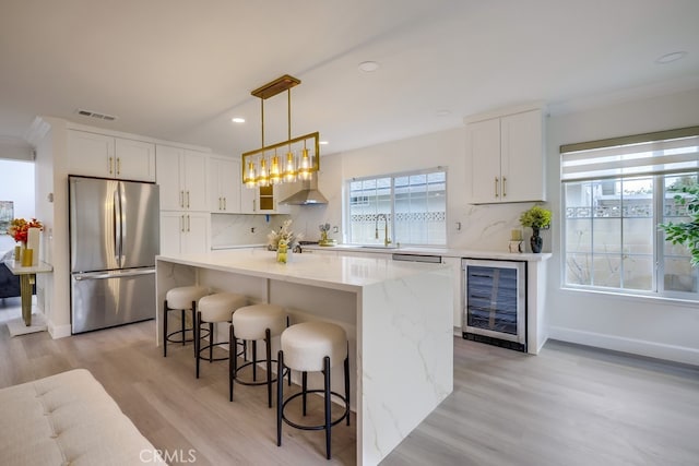 kitchen with pendant lighting, stainless steel refrigerator, white cabinetry, wine cooler, and wall chimney exhaust hood