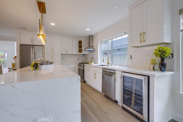 kitchen with appliances with stainless steel finishes, sink, wine cooler, hanging light fixtures, and wall chimney range hood