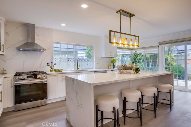 kitchen with white cabinetry, wall chimney range hood, stainless steel range with gas cooktop, and sink