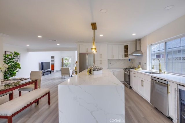 kitchen featuring appliances with stainless steel finishes, pendant lighting, tasteful backsplash, sink, and wall chimney range hood