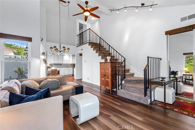 living room with dark hardwood / wood-style flooring, ceiling fan with notable chandelier, and a high ceiling