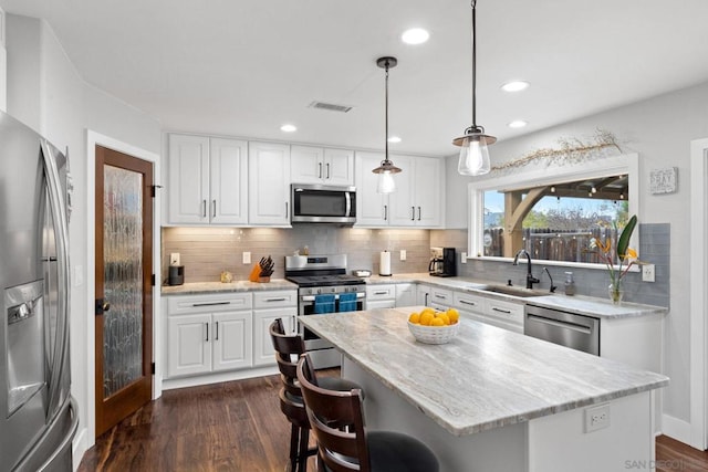 kitchen with stainless steel appliances, white cabinetry, a center island, and decorative light fixtures