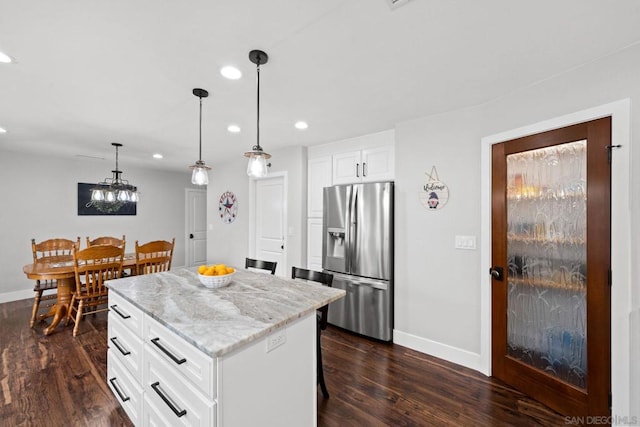 kitchen with decorative light fixtures, white cabinets, stainless steel fridge, a center island, and light stone countertops