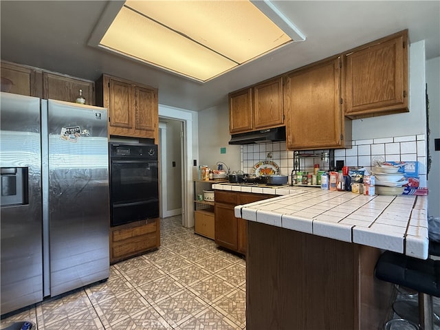 1490 W 51st St, Los Angeles, CA 90062 - kitchen featuring stainless steel refrigerator with ice dispenser, black oven, a warming drawer, tile counters, and under cabinet range hood
