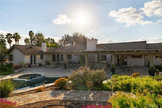 rear view of property featuring a patio area, french doors, and an in ground hot tub