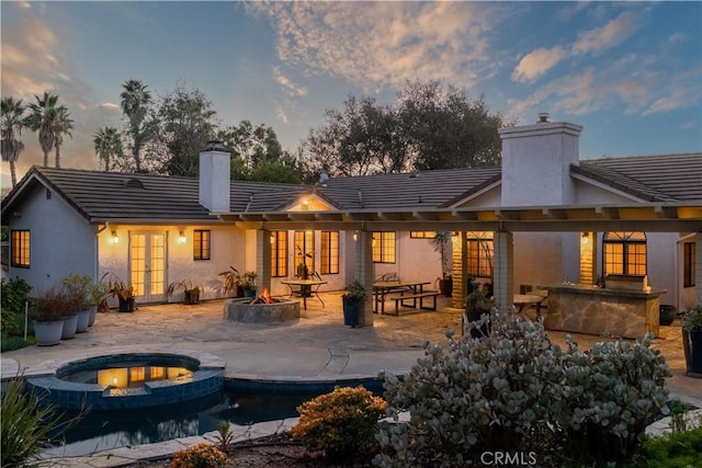 back house at dusk with exterior bar, an in ground hot tub, a patio, and an outdoor fire pit