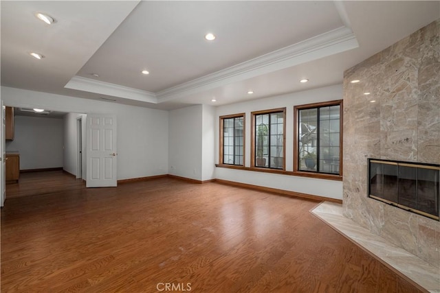 unfurnished living room featuring hardwood / wood-style flooring, a fireplace, a raised ceiling, and crown molding