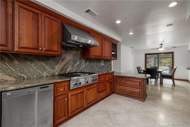 kitchen with appliances with stainless steel finishes, kitchen peninsula, stone counters, wall chimney range hood, and backsplash