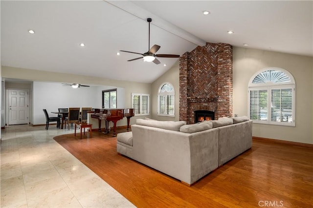 living room featuring ceiling fan, plenty of natural light, beam ceiling, and a brick fireplace