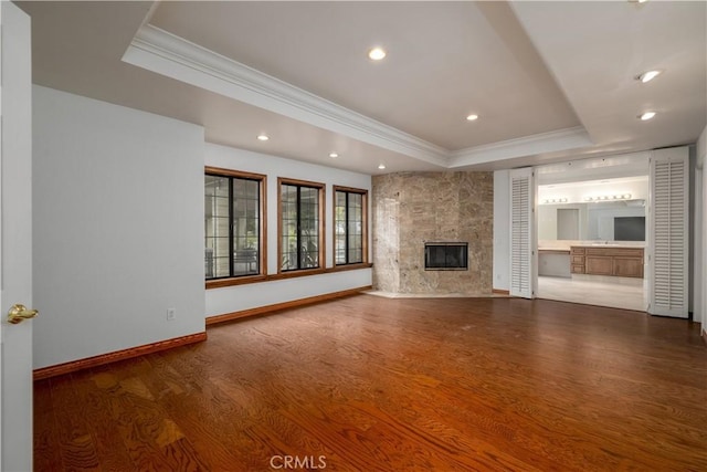 unfurnished living room featuring crown molding, hardwood / wood-style flooring, a fireplace, and a raised ceiling