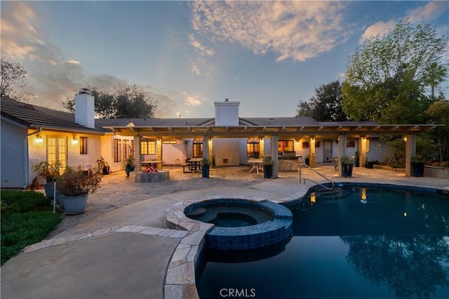 pool at dusk with an in ground hot tub and a patio