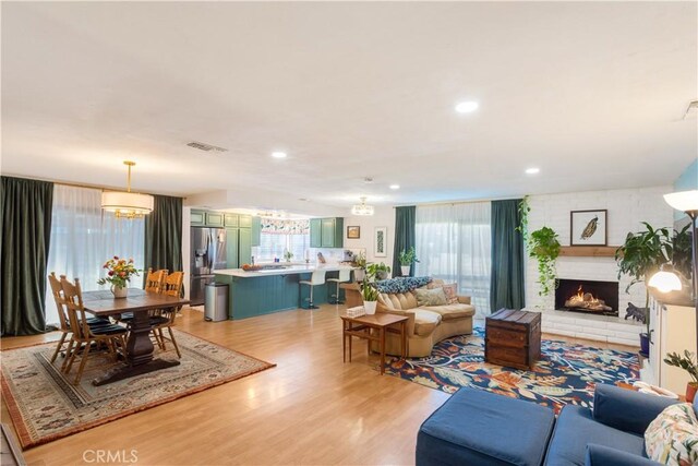 living room with an inviting chandelier, a fireplace, and light hardwood / wood-style floors