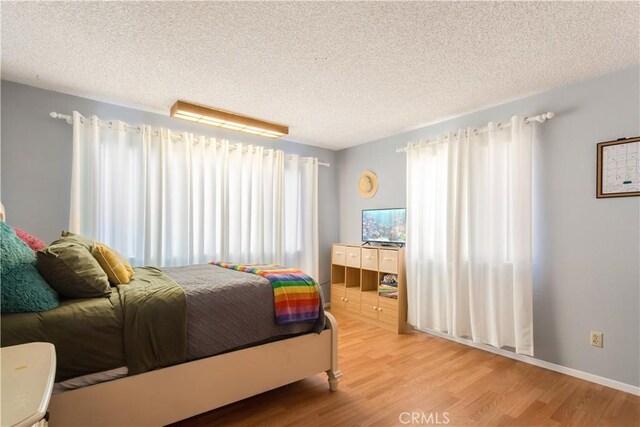 bedroom with a textured ceiling, wood finished floors, and baseboards