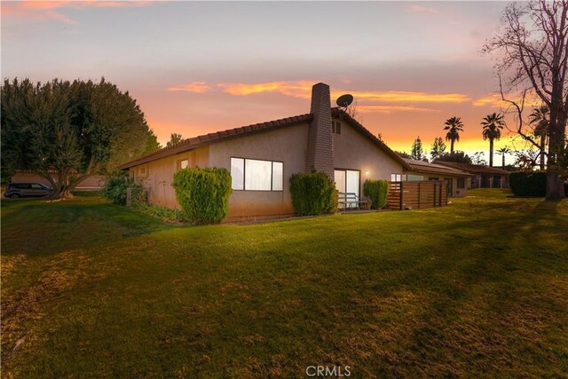 back of property at dusk with a yard, a chimney, and stucco siding