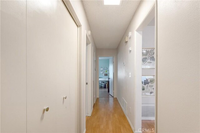 hall with visible vents, light wood-style flooring, and baseboards